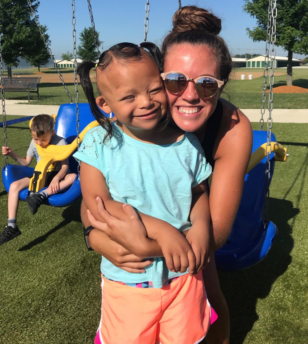 Adult woman and little girl posing for a picture in front of handicap swings.