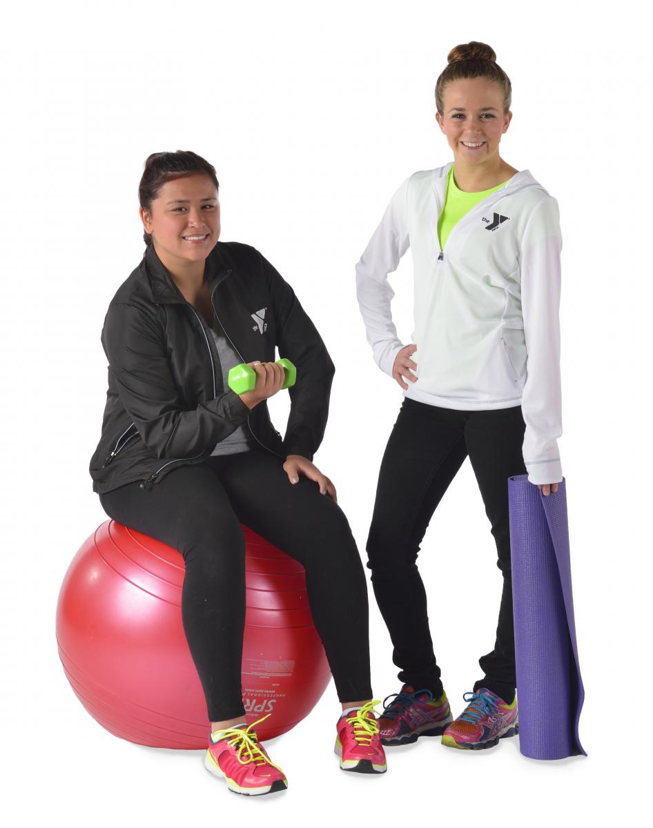 Two women posing with a yoga ball and yoga mat. 