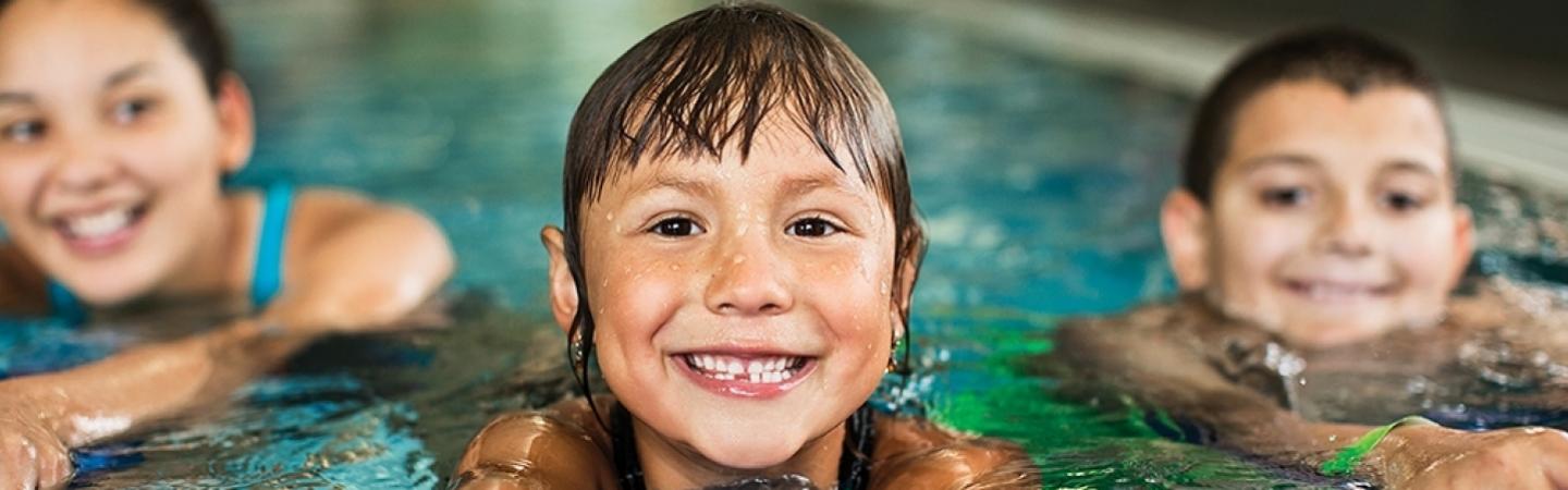 Three children in an aquatics pool smiling for camera.